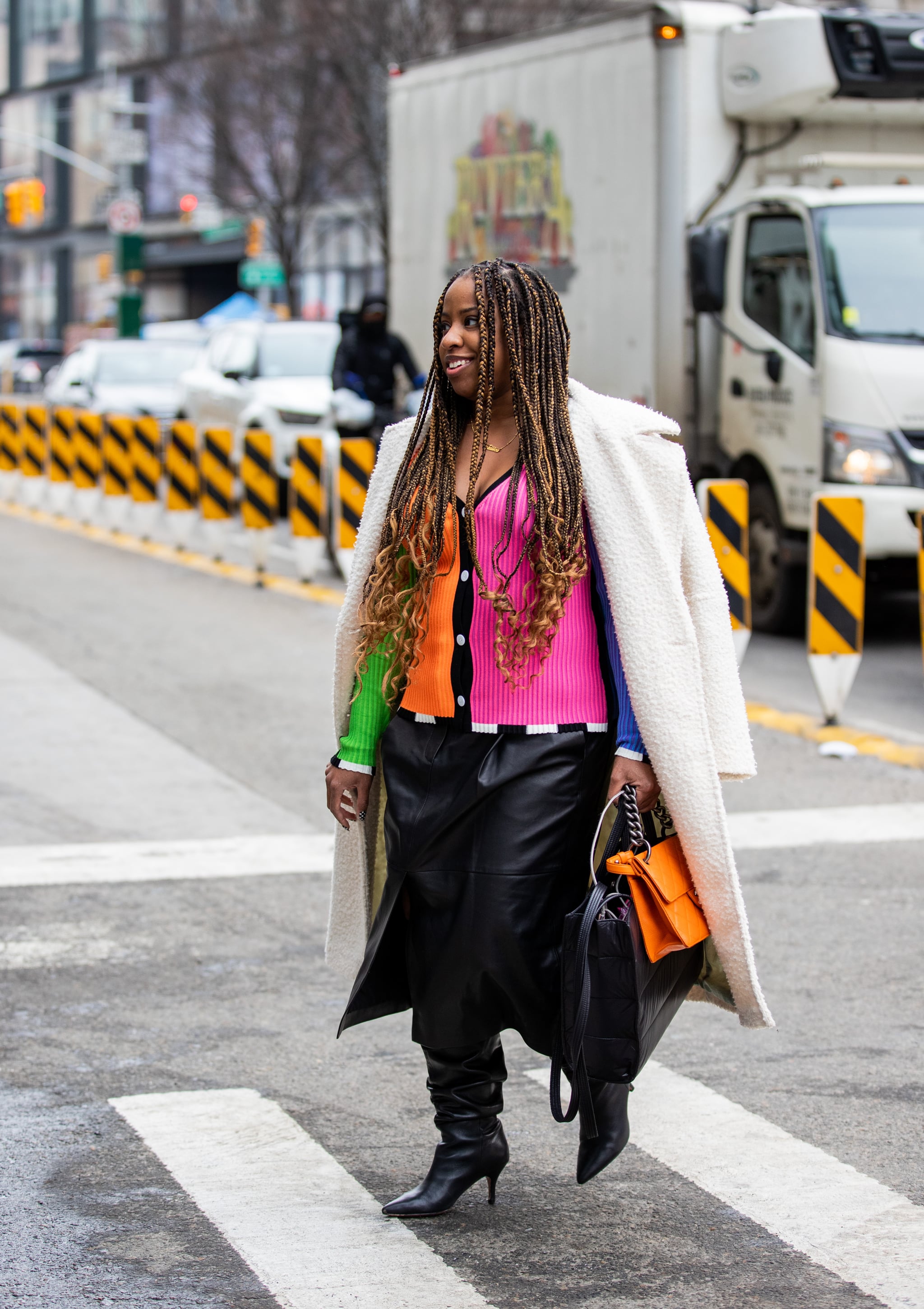 NEW YORK, NEW YORK - FEBRUARY 16: A guest is seen wearing multi colored button up top, black leather skirt, white coat, orange black bag, knee high boots outside Collina Strada during New York Fashion Week on February 16, 2022 in New York City. (Photo by Christian Vierig/Getty Images)