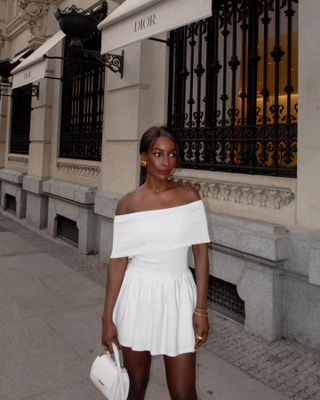 Influencer wears a white handbag with a white mini off the shoulder dress.