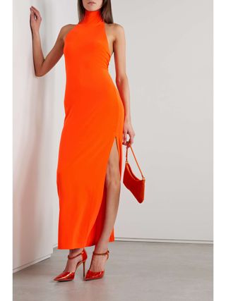 Norma Kamali turtleneck dress in orange worn with red high heels and a matching bag.