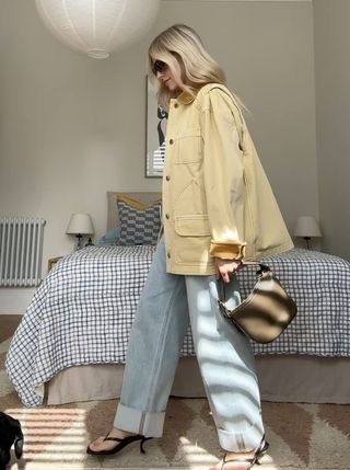 @joannalari wears a light yellow canvas jacket with blue turned-up jeans and a green top-handle bag