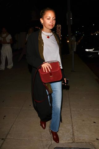 Nicole Richie styles a burgundy bag with jeans, a t-shirt, burgundy shoes, and a black long coat.