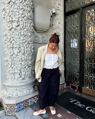 Marina Torres wearing a tan blazer, white embroidered top, navy pants, and white Margiela Tabi flats.