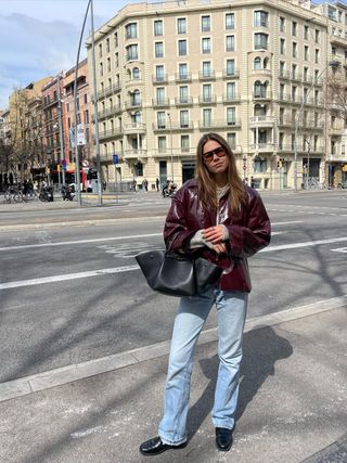 Fashion influencer @lunaisabellaa wearing a burgundy leather jacket, faded blue jeans, and trendy tinted aviator sunglasses.