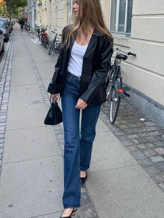 Fashion influencer @claradyrhauge on the street wearing. a black leather blazer, blue jeans, white tank, and sling-back pumps.