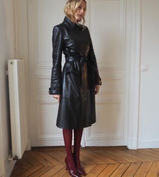 Stylist Elly McGaw in Paris wearing a black leather trench coat, burgundy tights, and burgundy pumps.