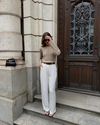 Woman wears camel knit and white tailored trousers