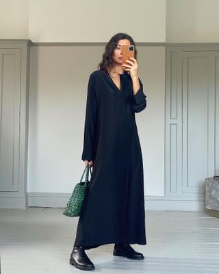 British influencer Marianna Smyth poses for a mirror selfie wearing a satin navy maxi shirtdress, green Dragon Diffusion, and flat black boots