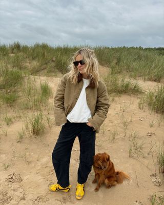 Lucy Williams wearing an olive barn jacket with black jeans and Onitsuka Tiger yellow Mexico 66 sneakers.