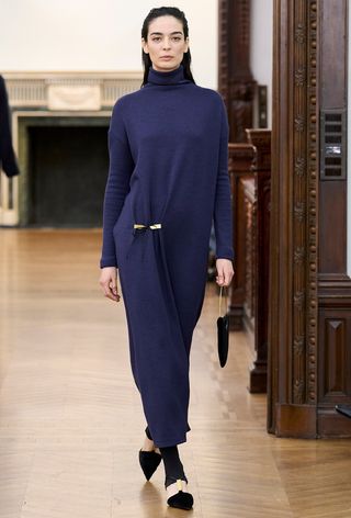 The navy color trend shown on Bevza's fall runway worn by a model wearing a navy turtleneck dress with gold hardware styled with black heels