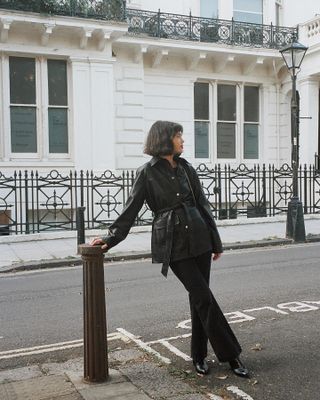 Influencer wearing black leather jacket and black jeans, standing on street taking outfit picture.