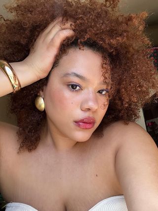 Ana Rivera with red curls, clear skin, and gold statement jewelry