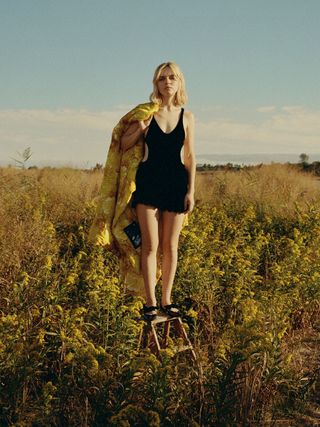 Odessa Young wears black romper in a field of yellow flowers.