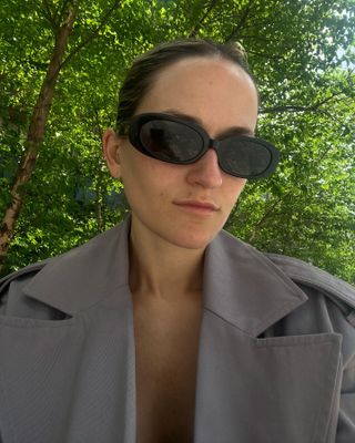 Eliza Huber wearing a gray trench coat and oval Linda Farrow sunglasses.