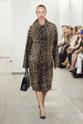 A Michael Kors Collection F/W 24 look on Amber Valletta including a leopard-print car coat with a black clasp bag and pumps.