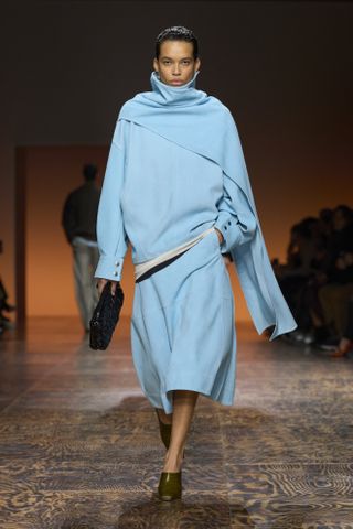 A turquoise F/W 24 Bottega Veneta look featuring a scarf-like cape top and matching A-line skirt with brown mules.