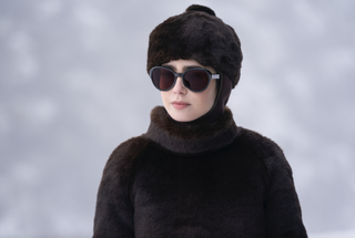 Lily Collins wears a fur coat and a fur hat with oversized sunglasses