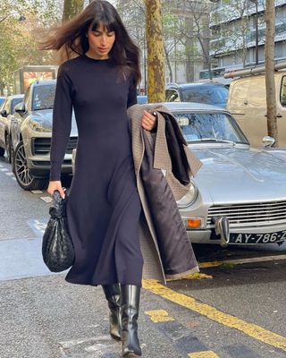 @tamaramory wearing a black dress and boots holding a coat