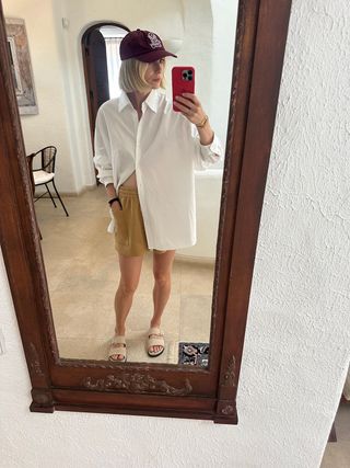 Varley's Lara Mead wearing tan shorts and an oversize white button-down with tan slide sandals.