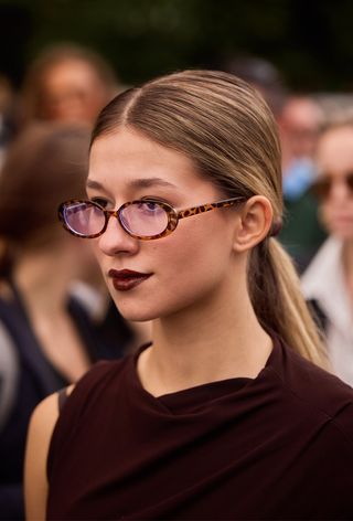 A woman wearing geek chic trend with eyewear and red draped top during Milan Fashion Week spring/summer 2025.