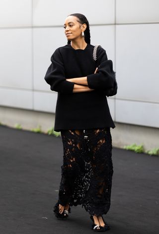 Solange Knowles wearing oversize jewelry with a black sweater, sheer black skirt, and black furry heels during Milan Fashion Week spring/summer 2025.