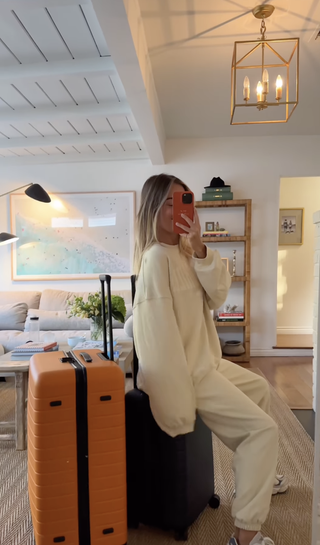 Photo of Daily Drills co- founder Mary Ralph Lawson sitting on top of luggage wearing white sweat set.