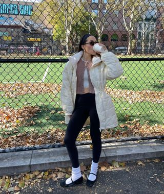 Anna wears an ivory puffer jacket, brown cardigan, white shirt, black leggings, white socks, and black Mary Janes.