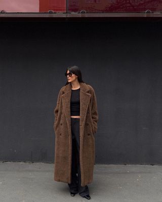 Woman wears brown teddy coat, black T-shirt, black trousers and black boots