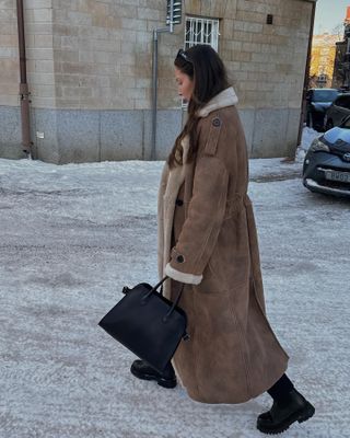 Woman wears brown shearling coat and black boots