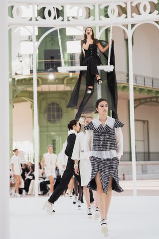 Riley Keough sitting on a swing in the Grand Palais wearing all black Chanel at the Spring Summer 2025 runway show singing 