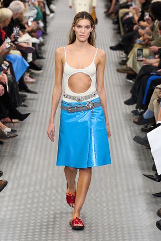 A model wearing a cream-and-white cut-out one-piece swimsuit and electric blue patent leather midi skirt at the Miu Miu spring summer 2025 runway show in Paris.