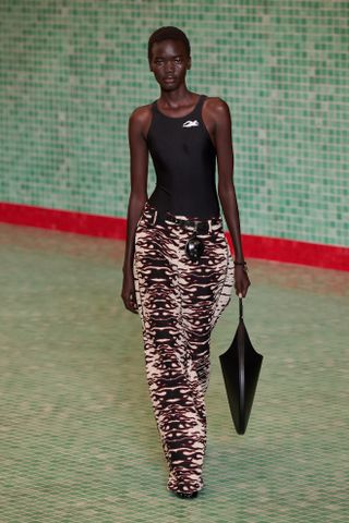 A Tory Burch model walks the spring/summer 2025 runway wearing a black swimsuit-inspired bodysuit and animal-print pants.