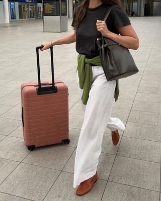 Woman wears white trousers, black T-shirt, brown loafers and black bag