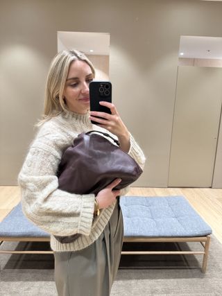 Woman wears beige knit, beige trousers and burgundy clutch bag