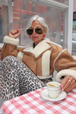 Woman wearing leopard print pants with a shearling jacket, red earrings, and aviator sunglasses.