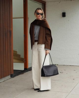 Woman in scarf coat and white pants.