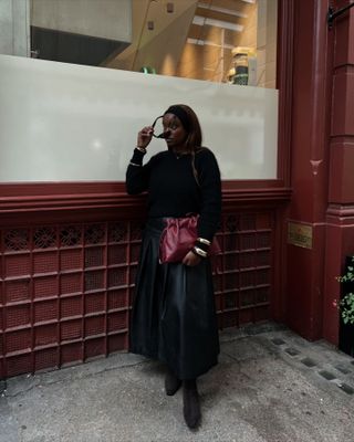 Elegant Jumper Outfits: @iamnkirote wears a black jumper with a black leather skirt and gold bangles