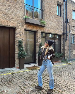 Sofia richie wears a black beanie, black leather jacket, blue jeans, and the Row's Zipped 1 boots in brown suede.