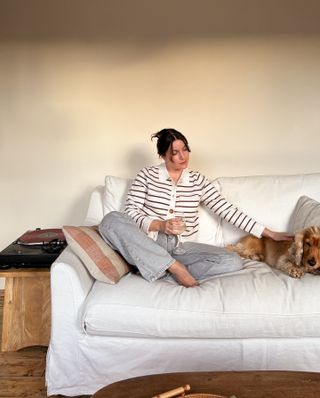 Woman wearing striped Sezane cardigan with blue jeans, sitting on couch.