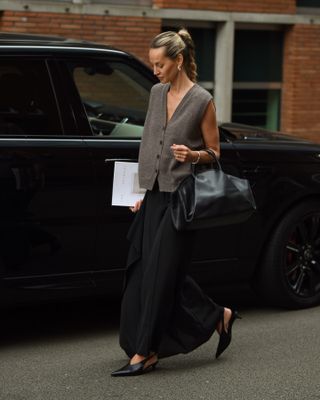 Woman wears sweater vest, handbag, black skirt and shoes