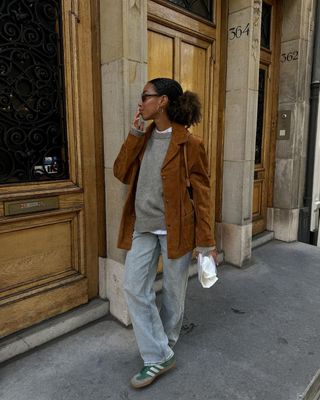 fashion influencer Amaka Hamelijnck wearing a brown suede jacket, relaxed jeans, and green suede Adidas Sambas