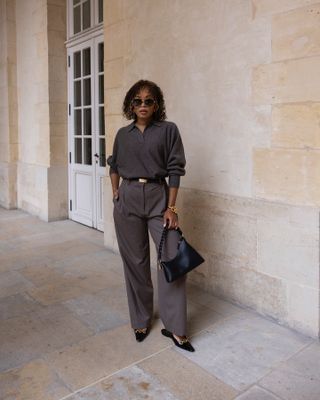 Influencer wears an outfit in a warm grey colour whilst walking on the street