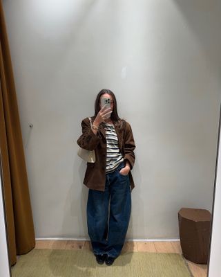 Woman in fitting room wearing dark jeans, striped t-shirt, and suede jacket.