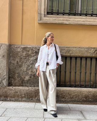 Woman standing on street wearing whit t-shirt, white button-down, linen pants and black heels.