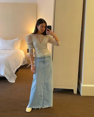 Influencer wears a lace blouse, maxi denim skirt, and white flats.