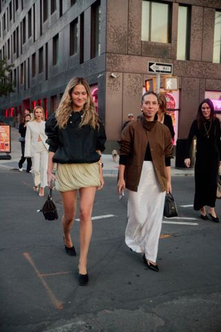 Who What Wear editors Eliza Huber and Lauren Eggertsen at the Tory Burch show. Huber is wearing a draped miniskirt with a black jacket.