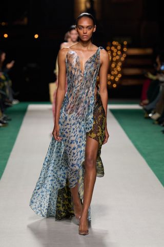 A model at the spring/summer 2025 Victoria Beckham show wearing a draped sheer floral dress with clear heels.