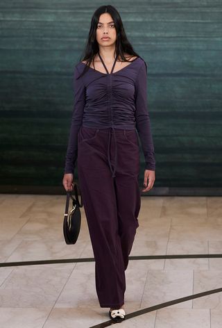 Model walking the OpéraSport runway show wearing a purple ruched top, purple denim, and flats.