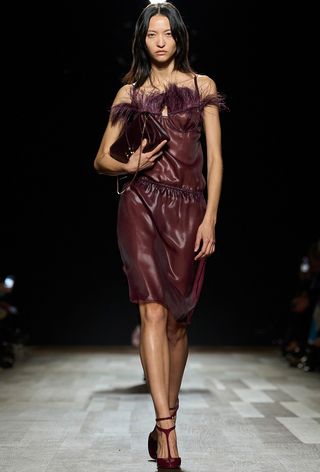 Model walking the Ferragamo runway show wearing a purple feather-trim top with a matching skirt and t-strap pumps.