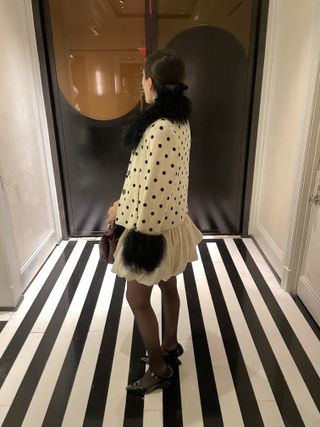 Anna wears a polka dot dress, sheer tights, and black flats.