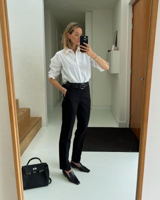 Anouk wears a white button-down shirt, black pants, black square-toe loafers, and a black belt.